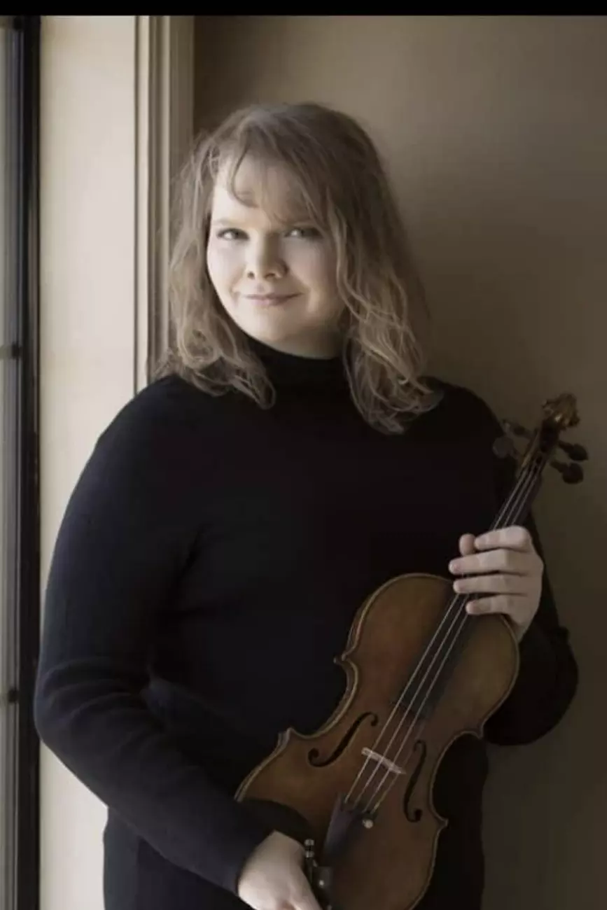 Violinist Sarah Beth Overcash holding her violin and smiling at the camera
