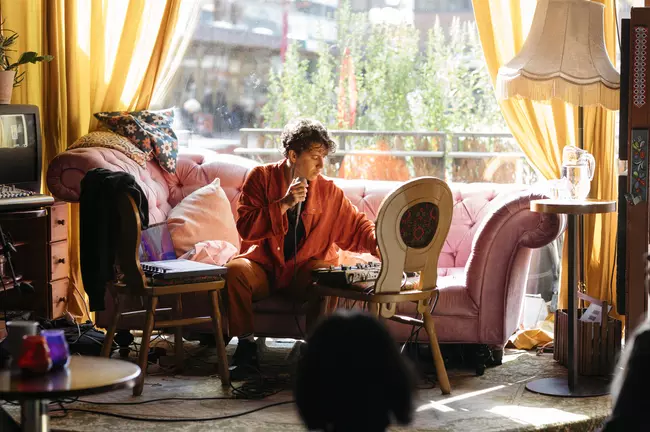 Musician performing, sitting on a couch in front of a large window