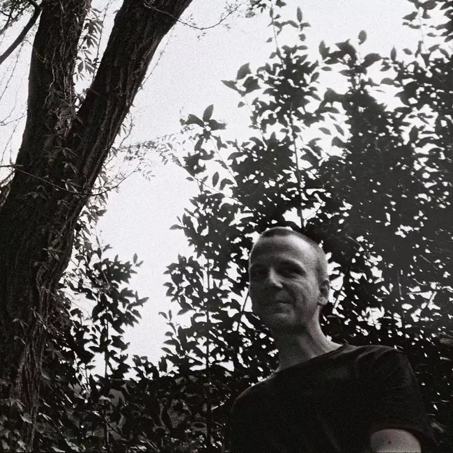 Lars Tuchel standing in front of a tree and smiling.