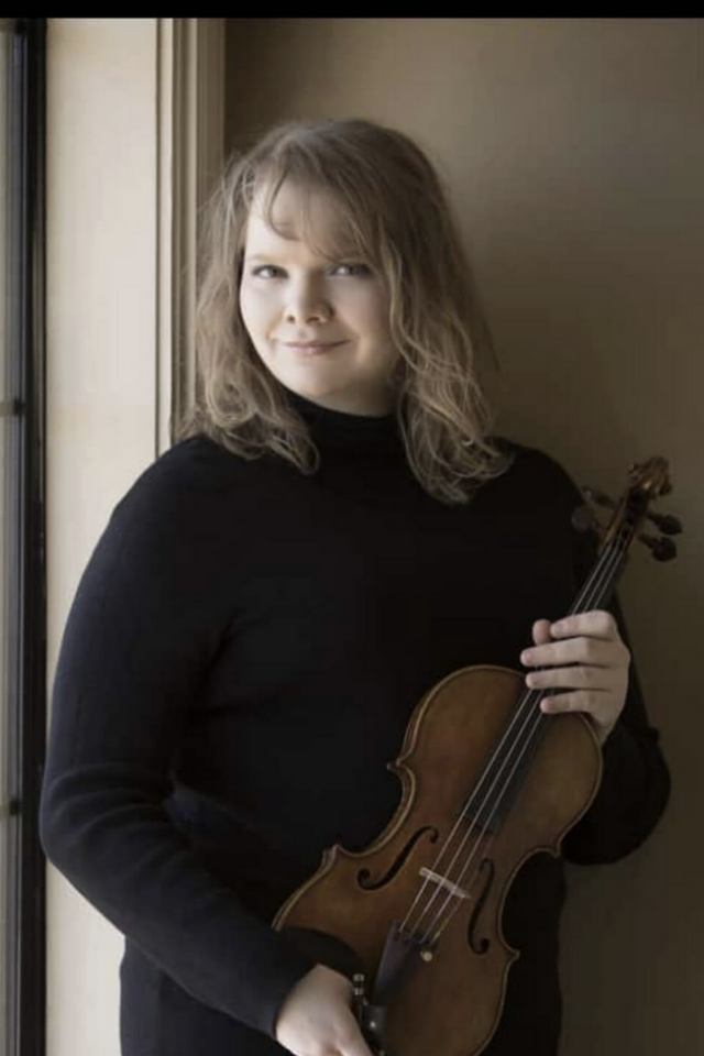 Violinist Sarah Beth Overcash holding her violin and smiling at the camera